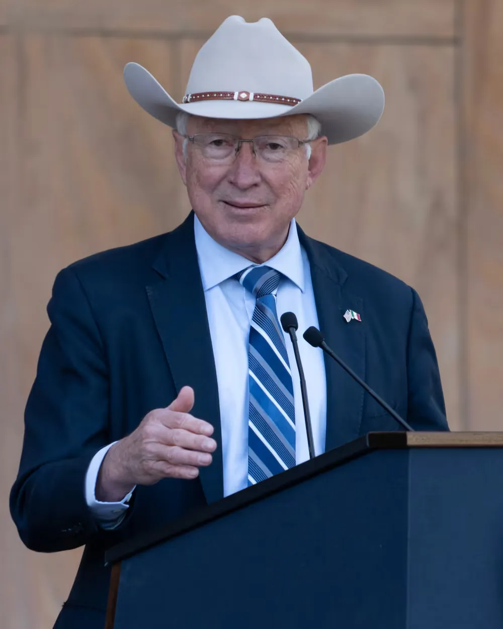 Ken Salazar in a suit and cowboy hat, speaking at a podium with both hands open
