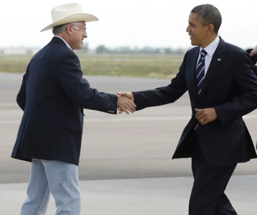 Ken Salazar in his cowboy hat shaking hands with President Obama on an airport tarmac