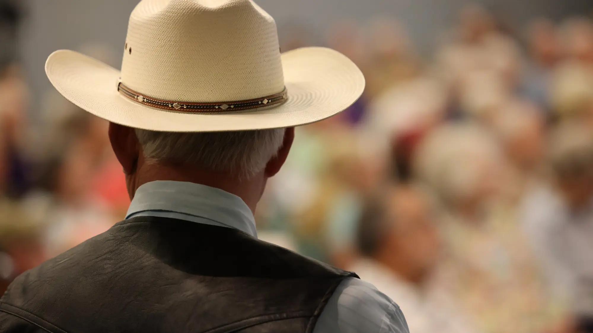Ken Salazar seen from behind in his cowboy hat, facing a full auditorium