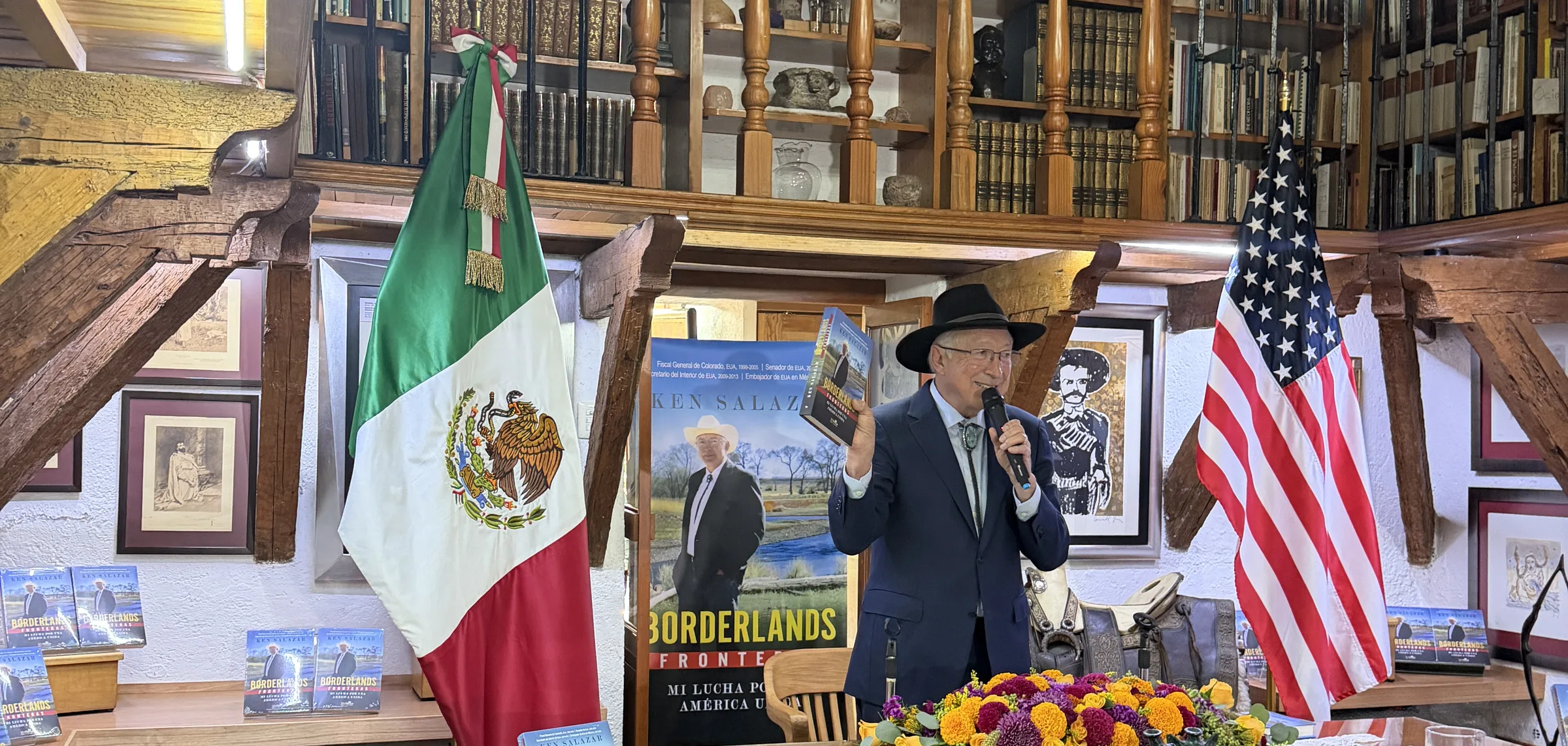 Ken Salazar holds up Fronteras between the Mexican and American flags at the Mexico City press conference